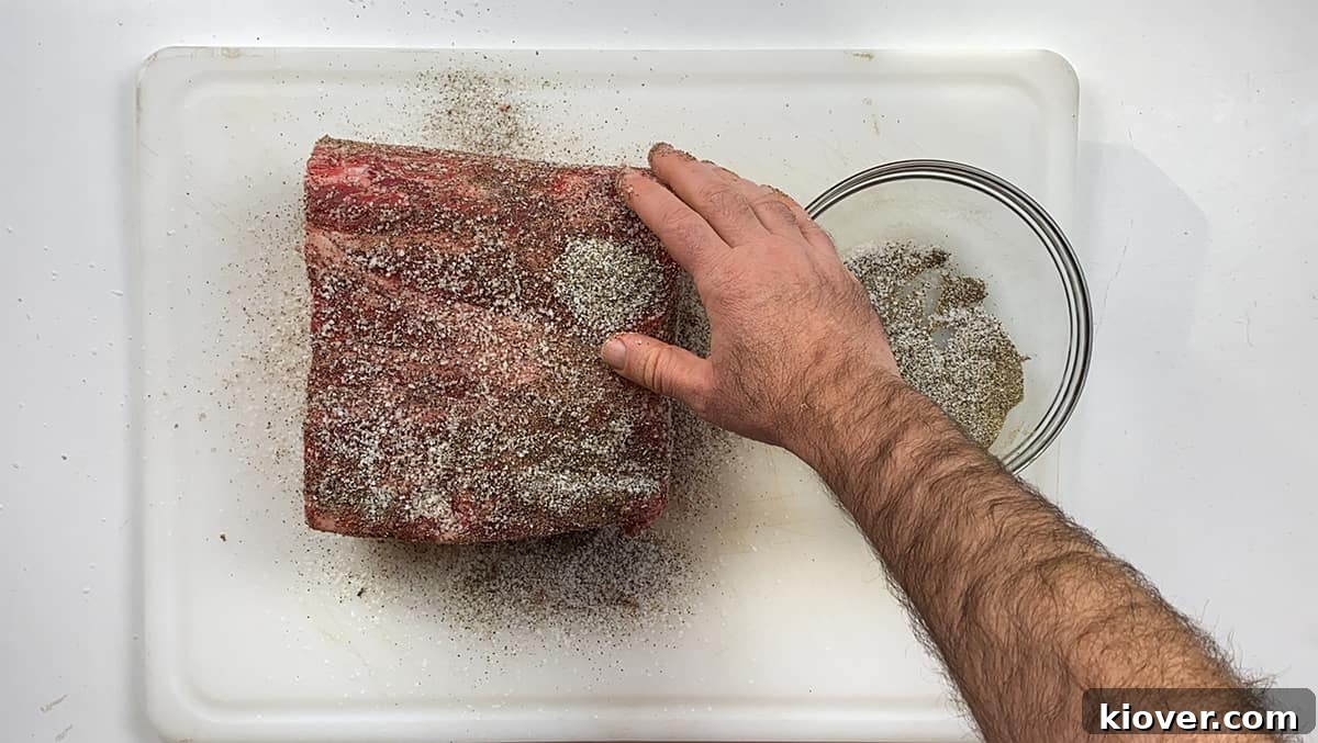 Season Roast A raw prime rib roast resting on a wooden cutting board, being generously rubbed with a mixture of salt and freshly ground black pepper, ensuring complete coverage before cooking.