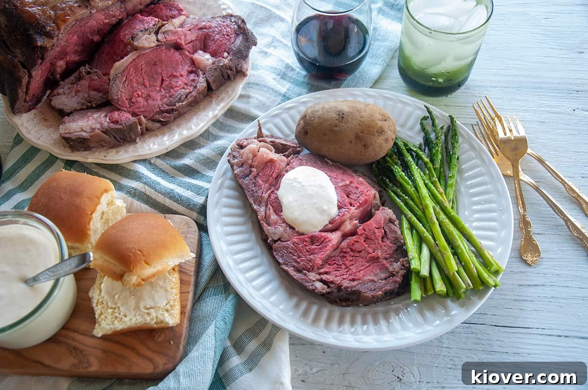 Sous Vide Prime Rib A grand spread featuring a sliced Sous Vide Prime Rib, beautifully arranged on a platter, accompanied by a plate with a serving of meat, fresh asparagus, a baked potato, and a bowl of the zesty horseradish sauce, all ready for a festive holiday meal.