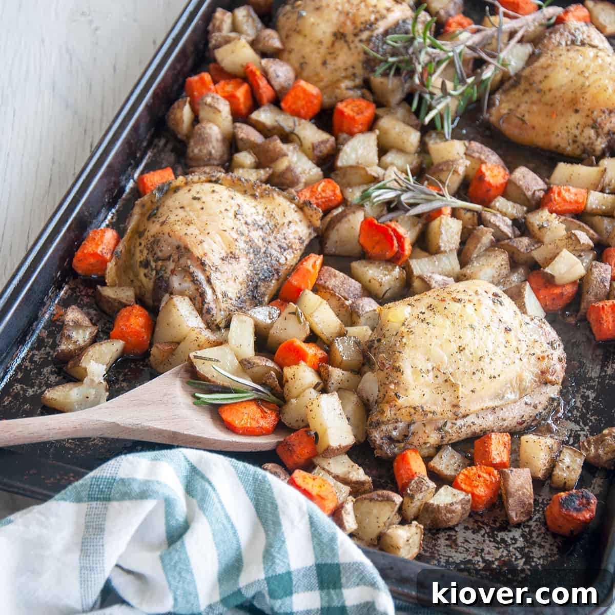 Baked Italian Chicken Thighs on a baking pan with carrots, potatoes, a wooden spoon and fresh rosemary.