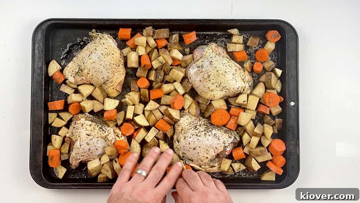 Chicken thighs, potatoes, and carrots all spread out on a baking pan.