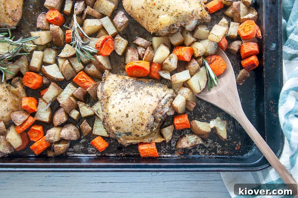 Four baked italian chicken thighs on a baking pan with potatoes and carrots.
