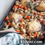 Baked Italian Chicken Thighs on a baking pan with carrots, potatoes, a wooden spoon and fresh rosemary.