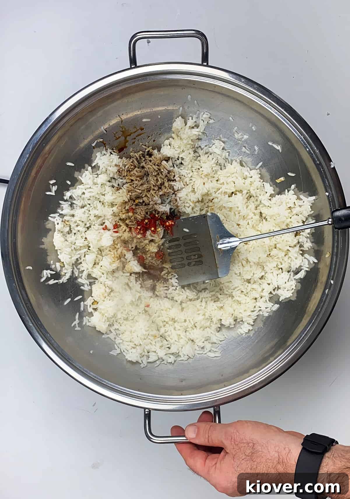 Vigorously stirring rice, pepper, and asian sauces in heated wok.