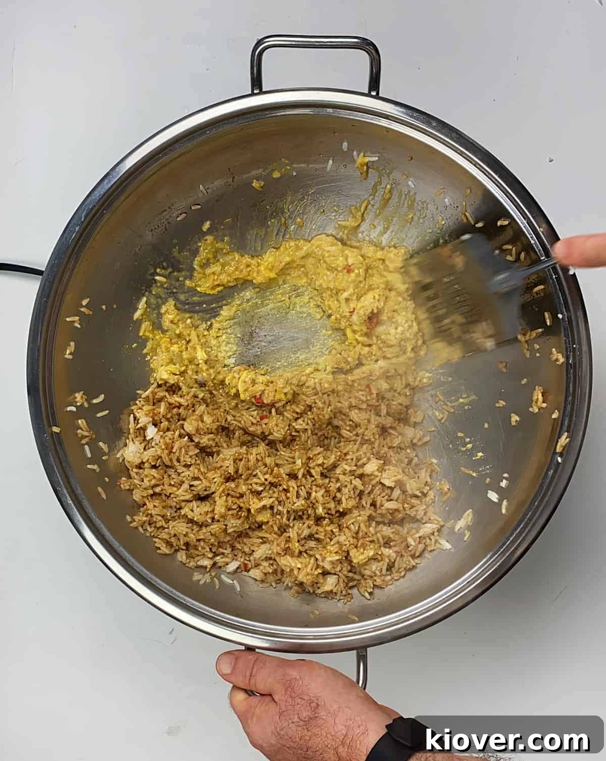 Vigorously stirring eggs in wok while rice is sitting on the side of a wok.