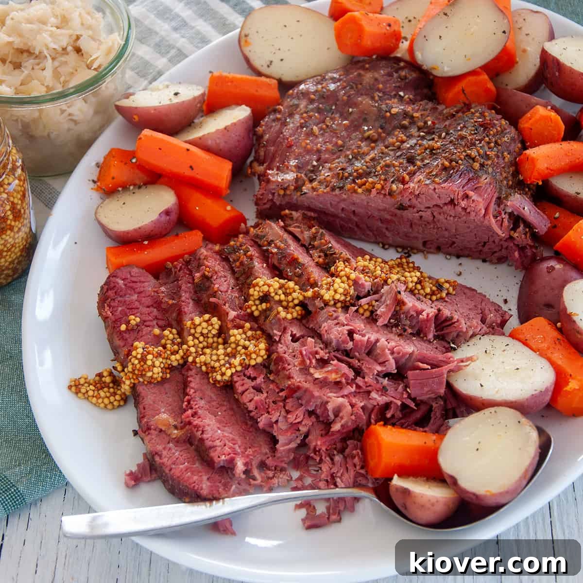 Full sous vide corned beef roast on a large serving platter with potatoes and carrots all around the sides of the roast.