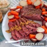 Full sous vide corned beef roast on a large serving platter with potatoes and carrots all around the sides of the roast.