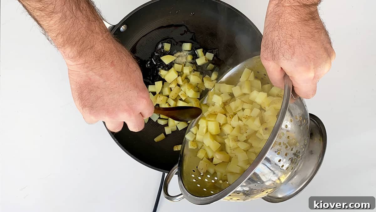 Crispy Homemade Corned Beef Hash 3 Parboiled potatoes are being poured into a sizzling frying pan filled with hot bacon grease, preparing for the crisping stage of the corned beef hash.
