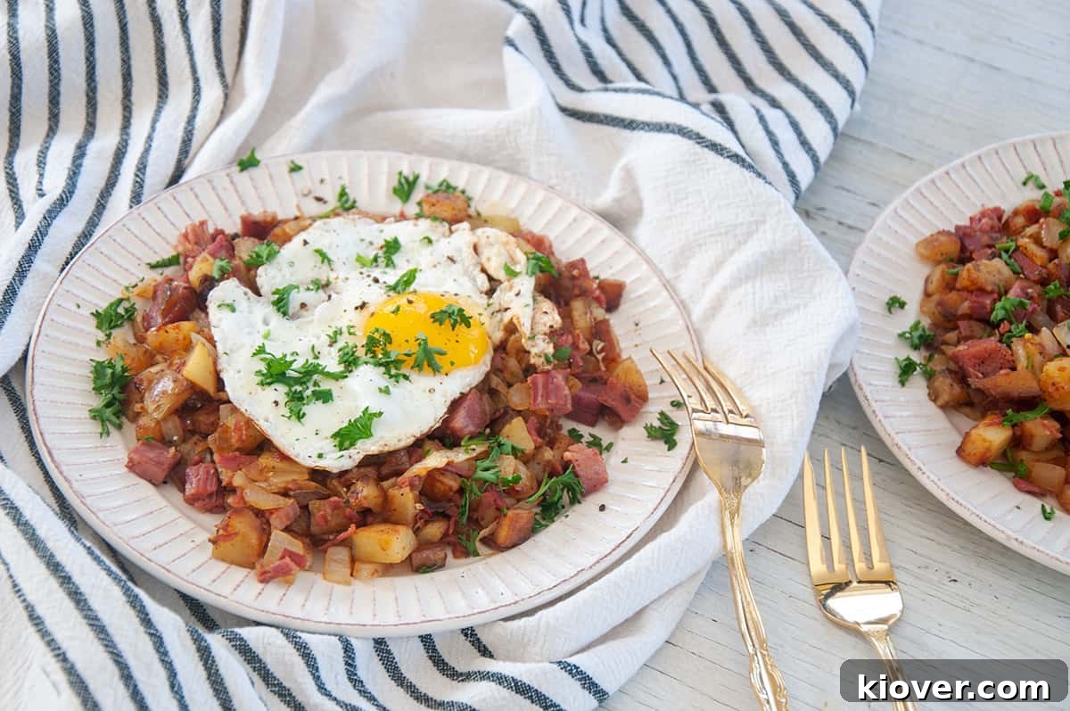 Crispy Homemade Corned Beef Hash 6 A serving of Corned Beef Hash adorned with a perfectly cooked sunny-side-up egg and fresh parsley, presented alongside two elegant gold forks.