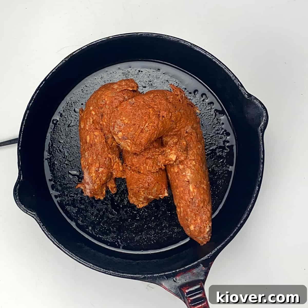 Chorizo in Pan Uncooked Mexican chorizo being added to a cast iron skillet.