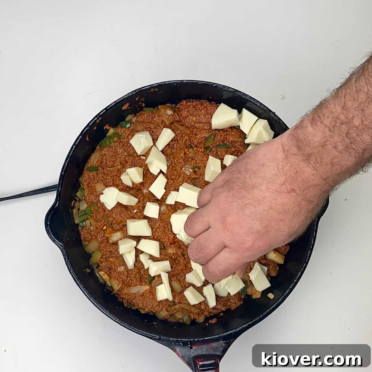 Adding Cheese A hand sprinkling shredded Oaxaca cheese over the cooked chorizo and vegetable mixture in a cast iron skillet.