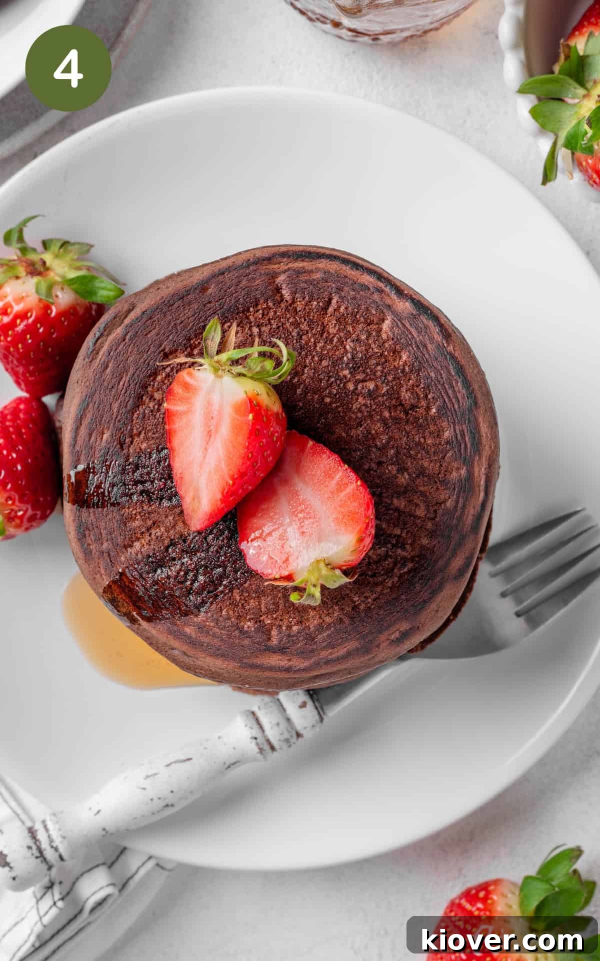 Decadent Chocolate Pancakes Recipe for Fluffy, Fudgy Stacks 7 pancakes garnished with fresh strawberries, and drizzled with maple syrup.