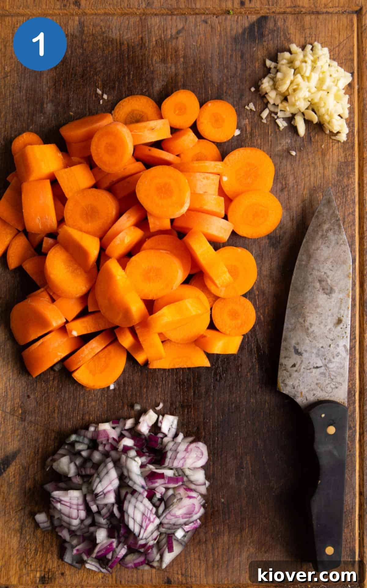Carrot and Coriander Soup Recipe — Creamy Spiced Carrot Soup 4 Chopped carrots, garlic, red onion on a wooden chopping board with a knife.