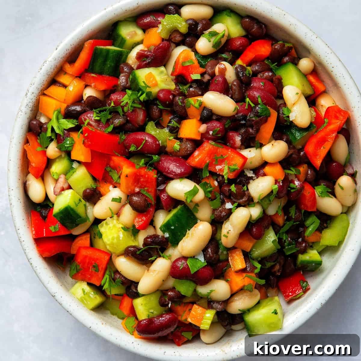 mixed bean salad topped with freshly chopped coriander in white/grey bowl on white surface.