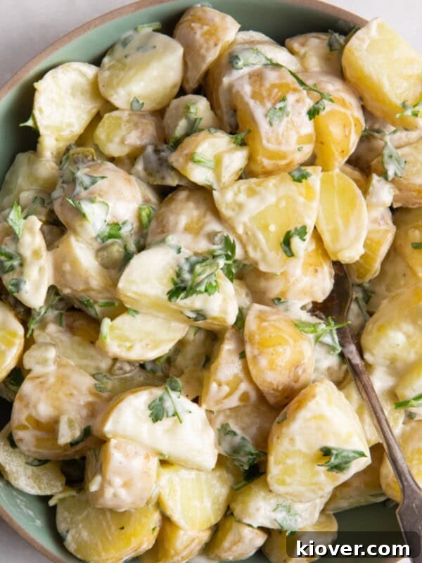 potato salad in green bowl with beige rim. Bowl is on white surface.