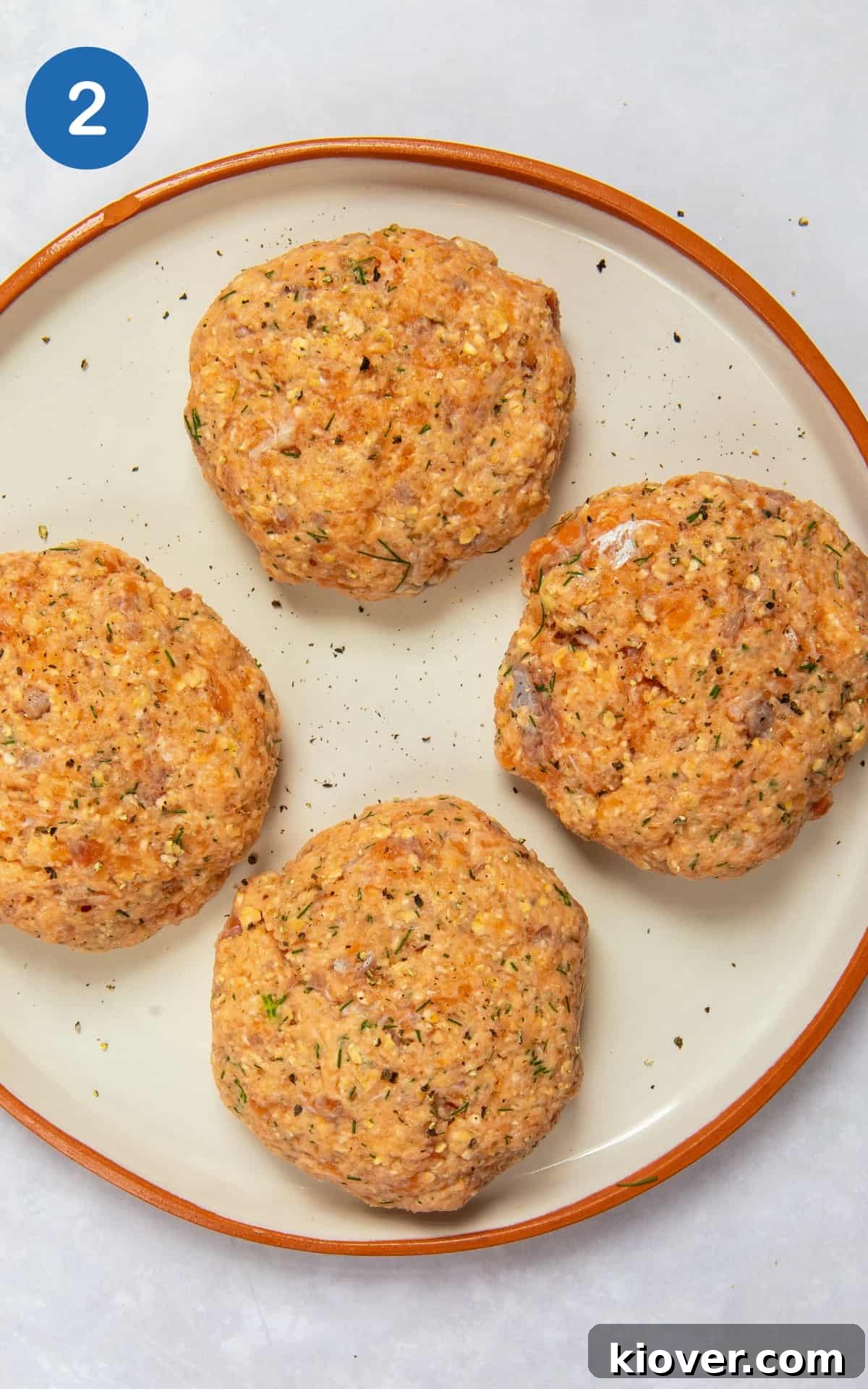 Grilled Salmon Burgers with Lemon-Dill Aioli 5 uncooked salmon burgers in patty shapes on white plate with orange rim.