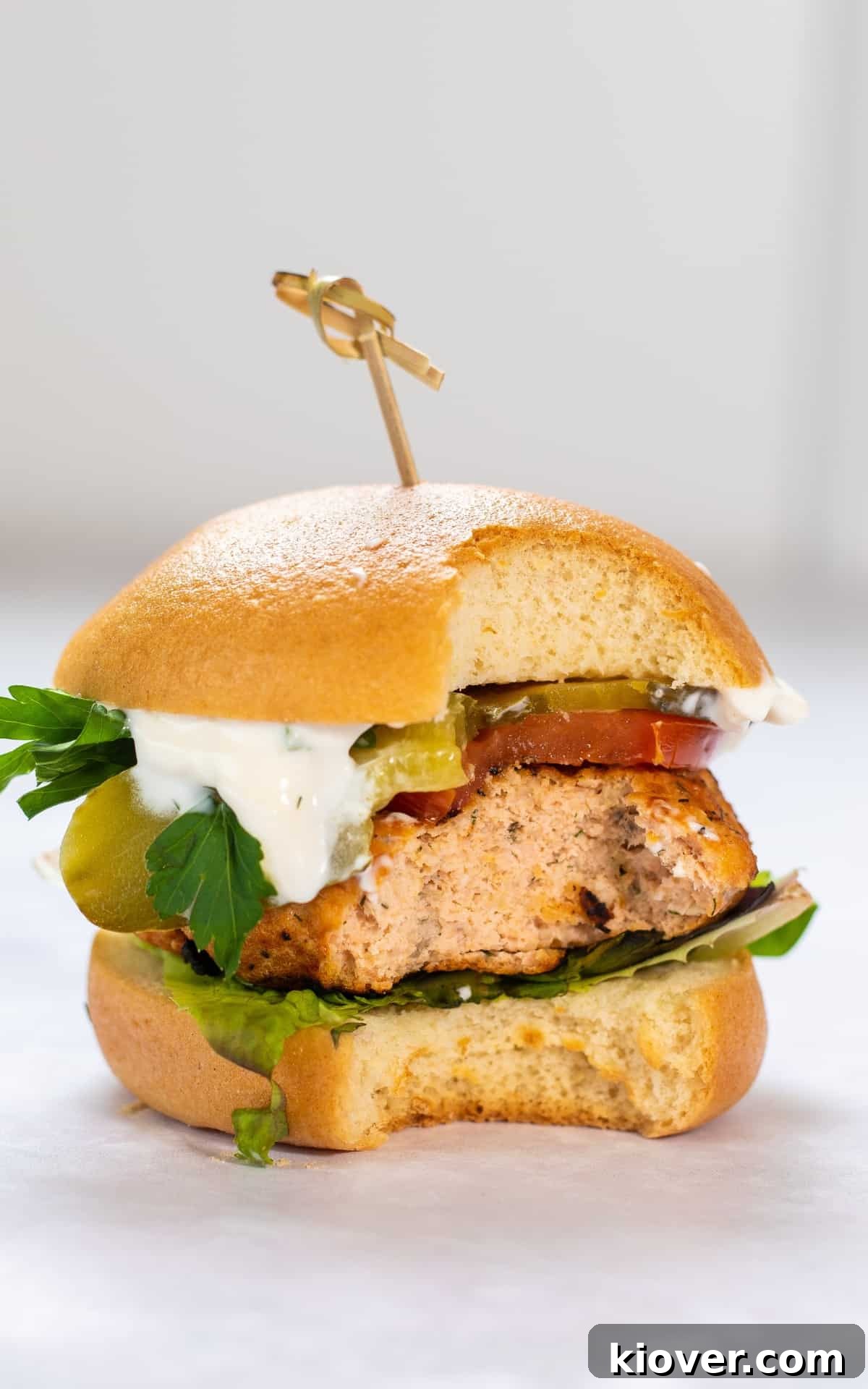 Grilled Salmon Burgers with Lemon-Dill Aioli 7 salmon burgers with bun and lettuce. Bite has been taken from the salmon burger.