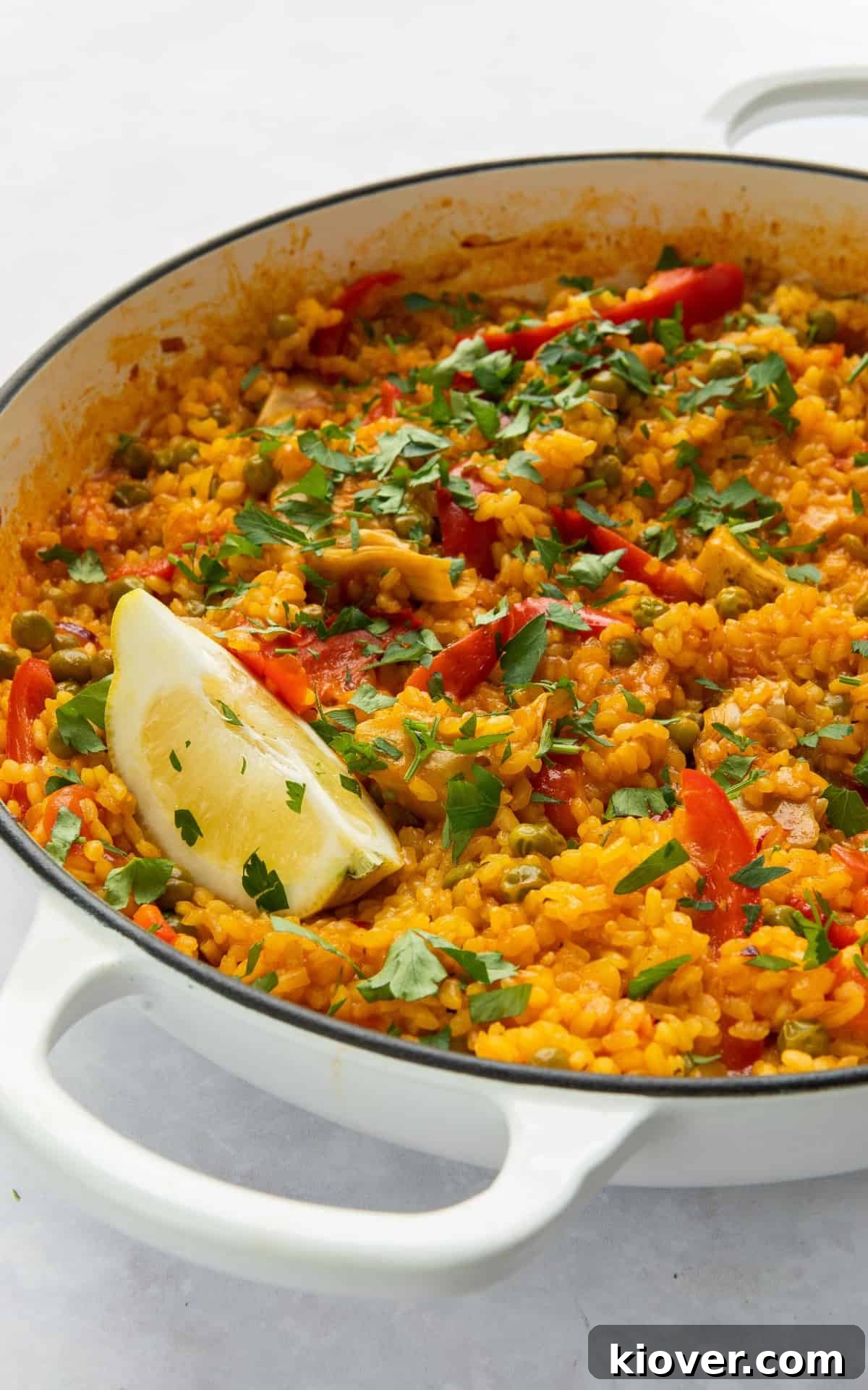 Vegetarian Paella Recipe: Flavorful Spanish Rice with Veggies 6 Paella in large white shallow dish with wedge of lemon.