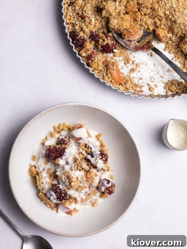 apple and blackberry crumble on a marble background served with cream.