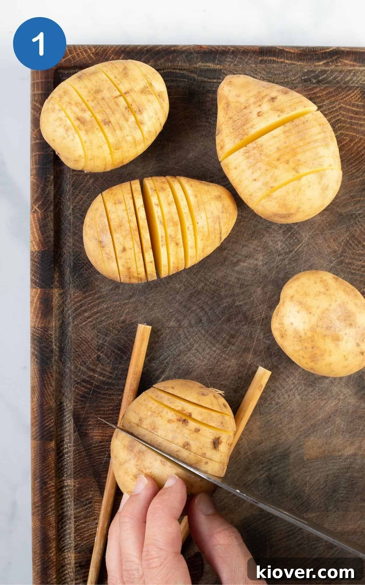 Crispy Hasselback Potatoes with Garlic and Parmesan 4 Sliced potatoes on a wooden chopping board.