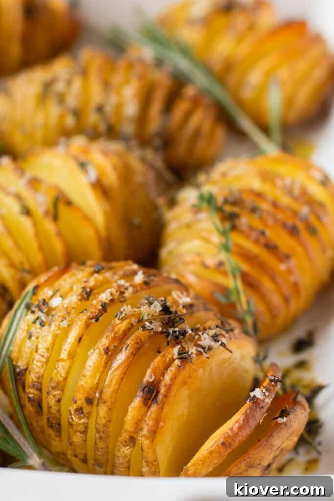 Crispy Hasselback Potatoes with Garlic and Parmesan 8 a closeup front view of these roasted potatoes seasoned with herbs, salt, and olive oil in a white baking dish.