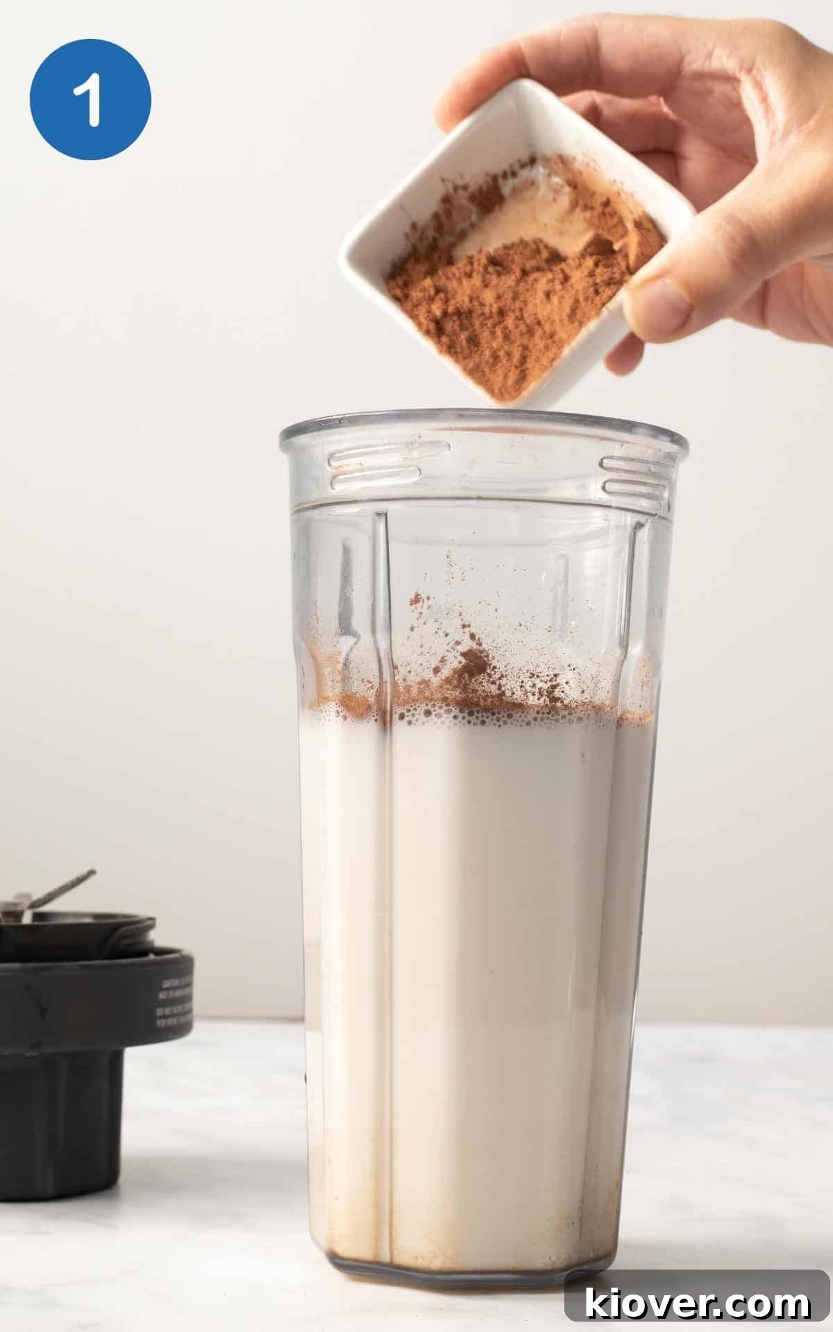 a side view of the author adding the spices and cacao powder to the milk in a blender.