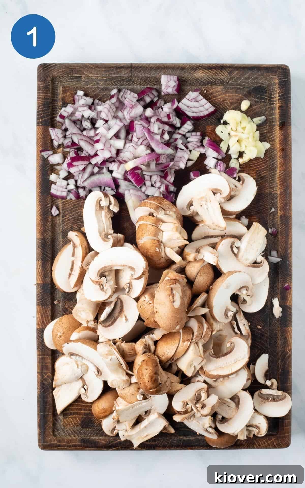 overhead view of diced garlic, Onion, and Mushrooms on a wooden chopping board.