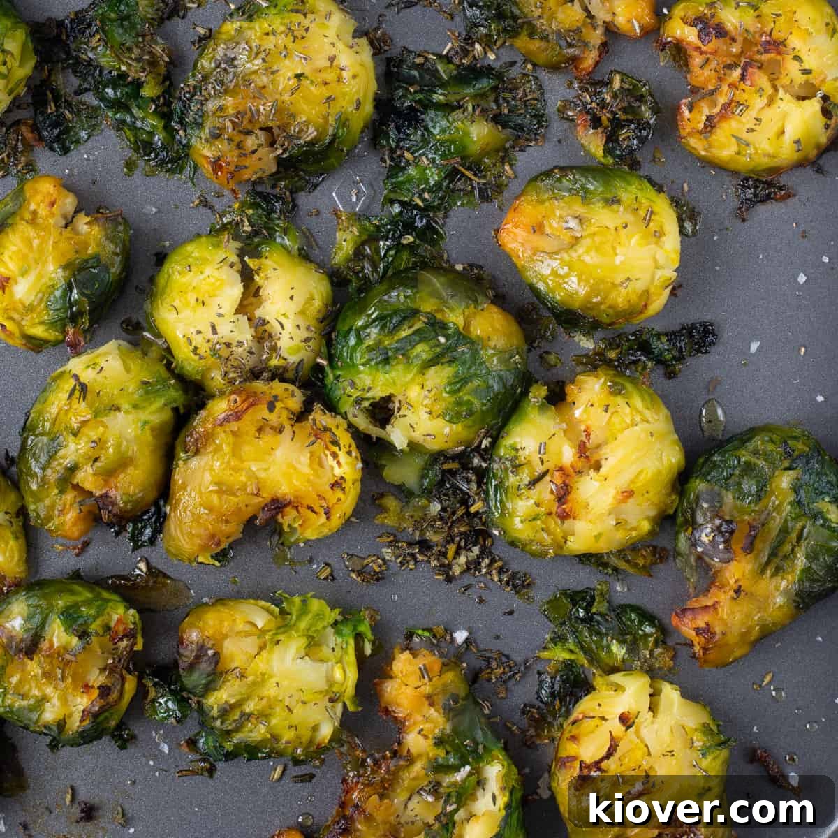Crispy Smashed Brussels Sprouts with Garlic and Parmesan 2 crispy brussel sprouts on grey baking tray with herbs on top.
