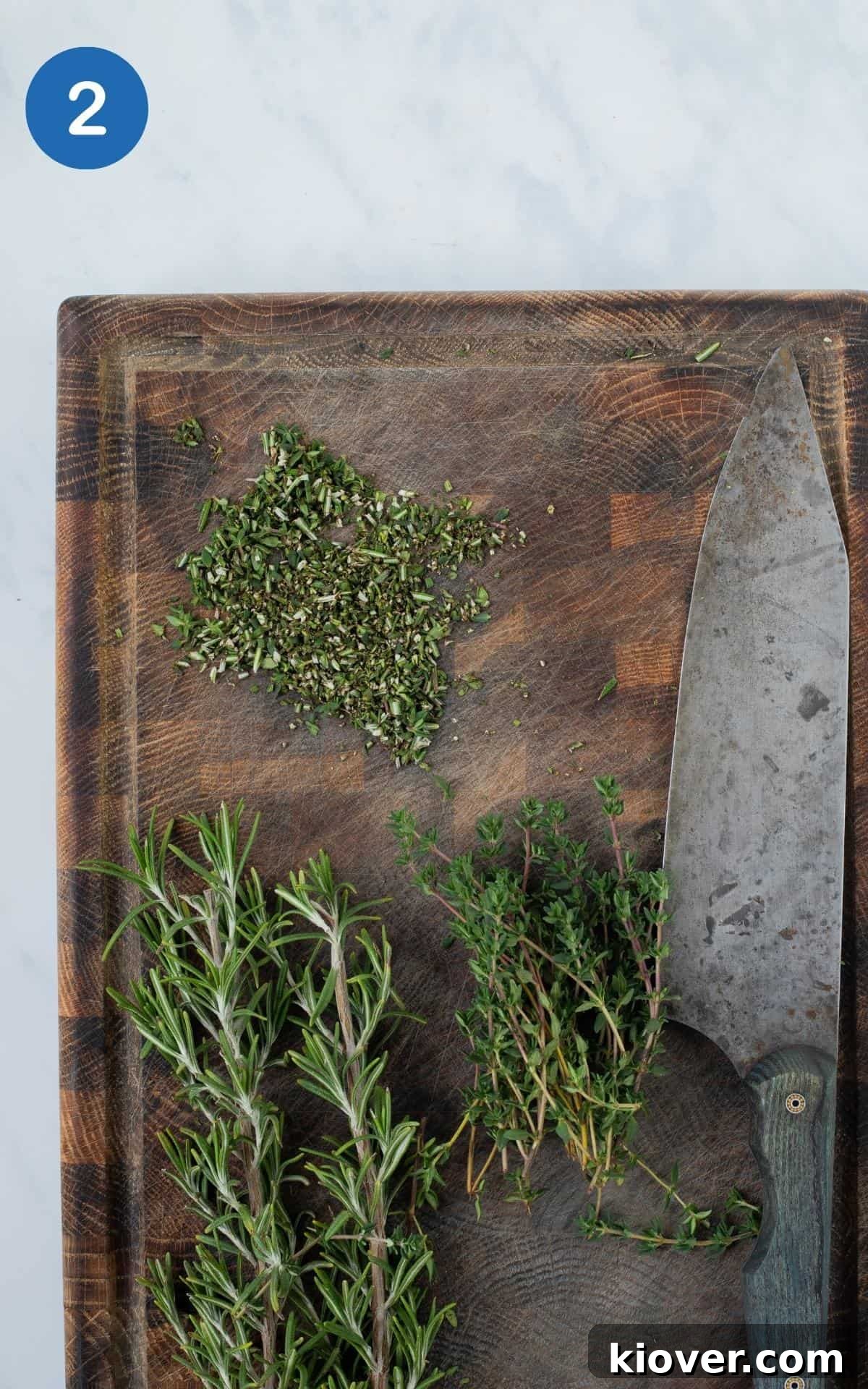 Crispy Smashed Brussels Sprouts with Garlic and Parmesan 5 rosemary and thyme finely diced on wooden chopping board with knife showing.