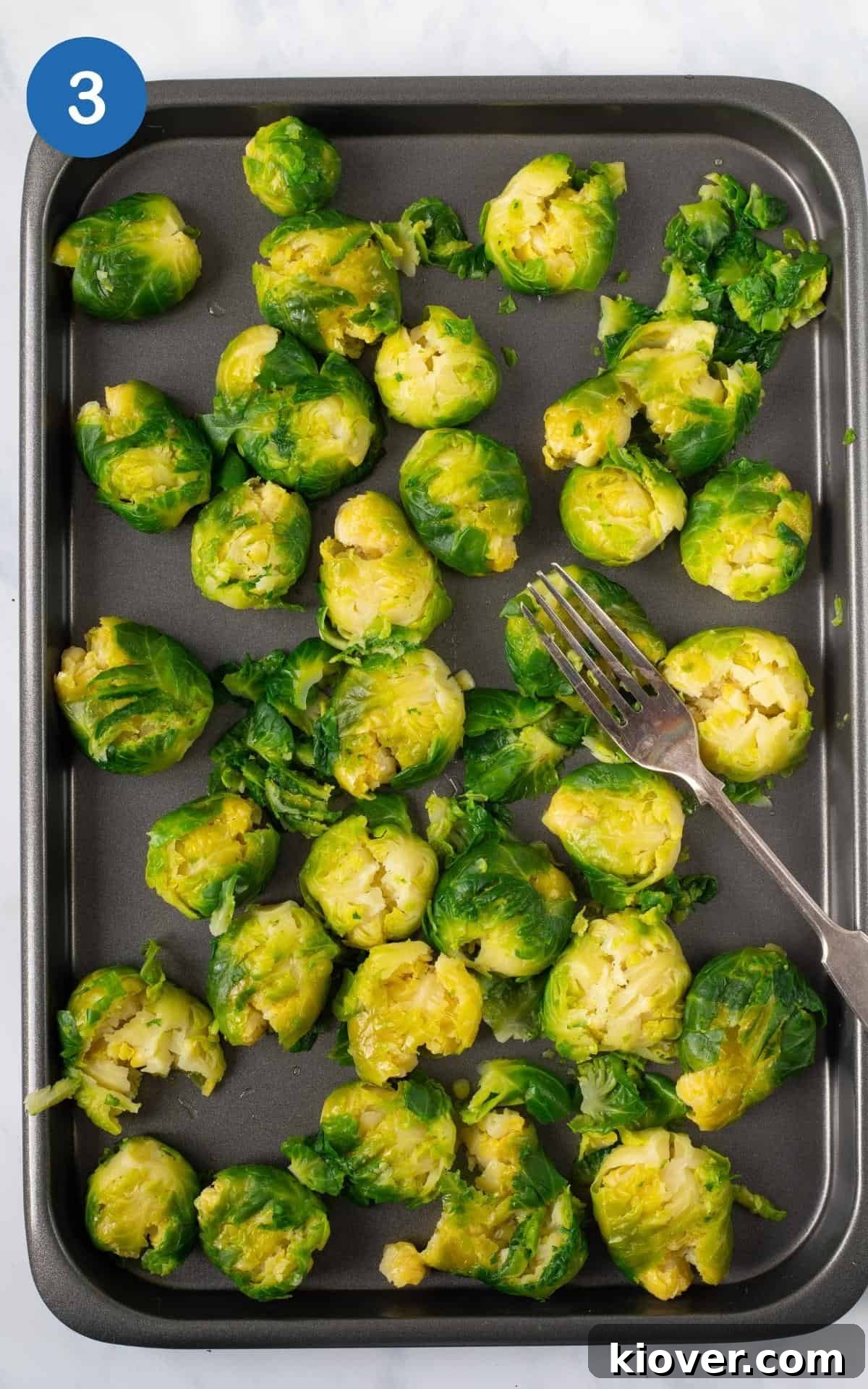 Crispy Smashed Brussels Sprouts with Garlic and Parmesan 6 boiled brussel sprouts smashed on baking tray being squash with a silver fork.