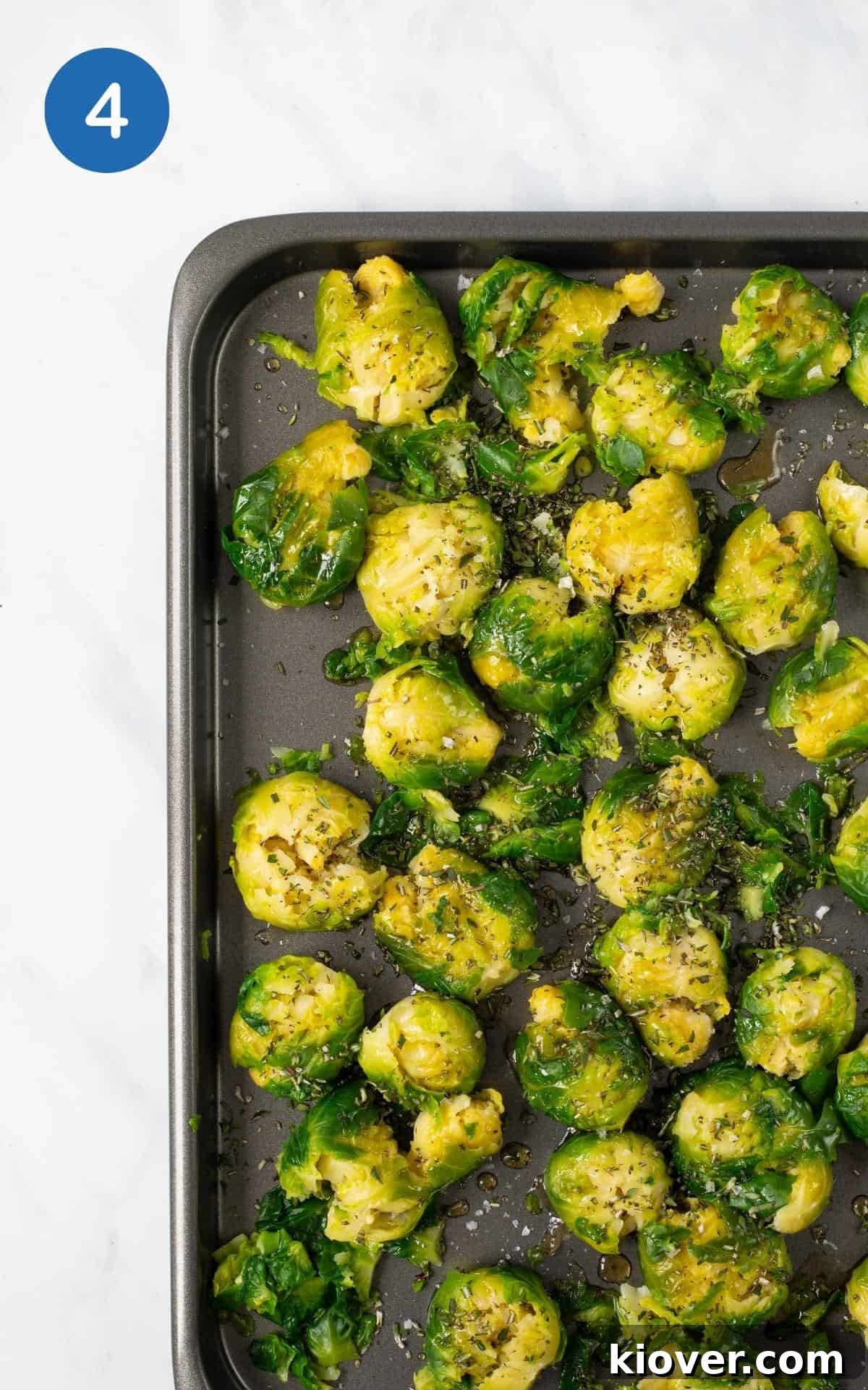 Crispy Smashed Brussels Sprouts with Garlic and Parmesan 7 smashed brussel sprouts on baking tray topped with olive oil, maple syrup, herbs, salt ready to be roasted.