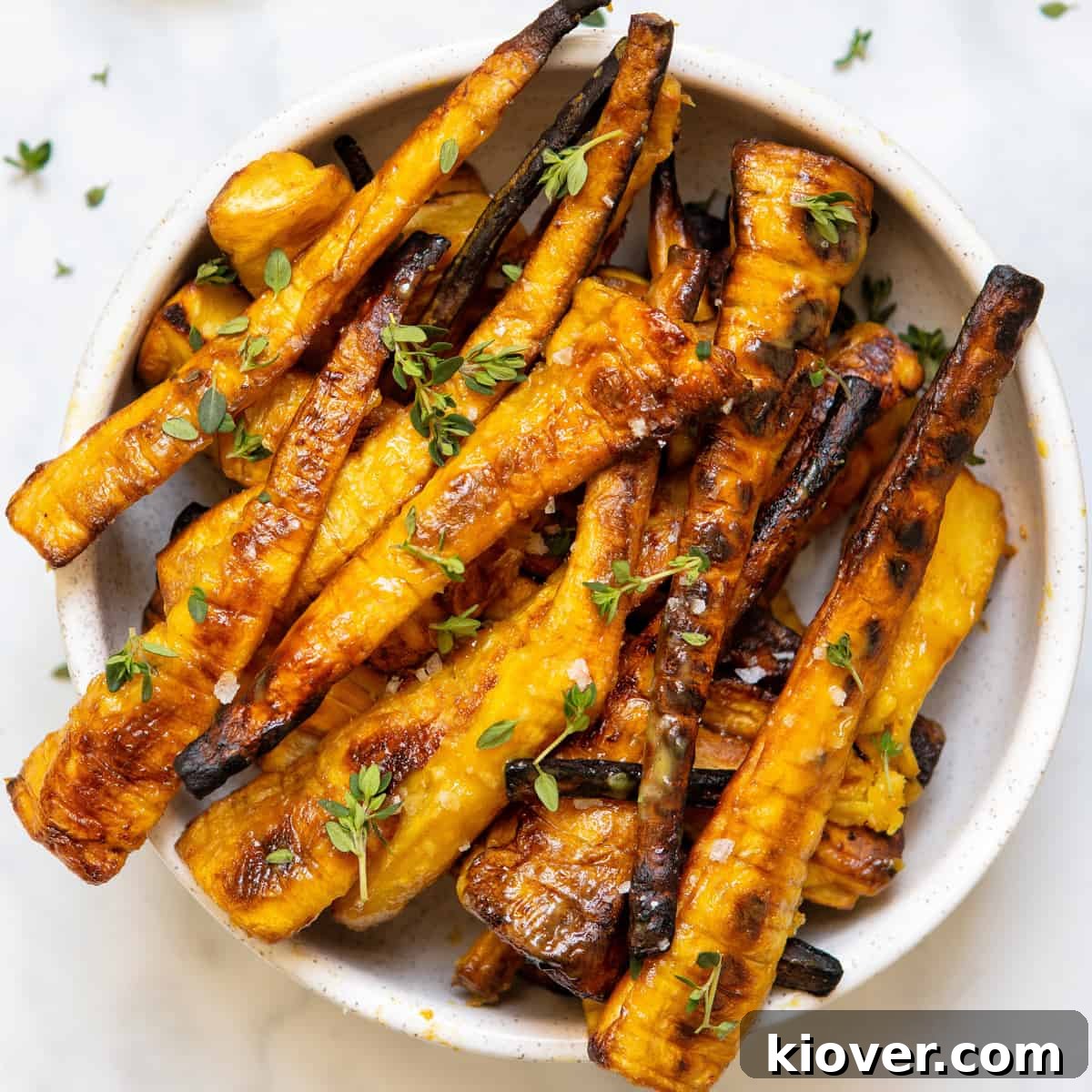 closeup of these mustard and maple glazed parsnips in a white bowl on backdrop with fresh thyme leaves.