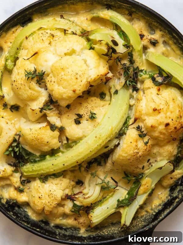 Cooked Cauliflower Cheese in black skillet pan. Pan is displayed on white marble background