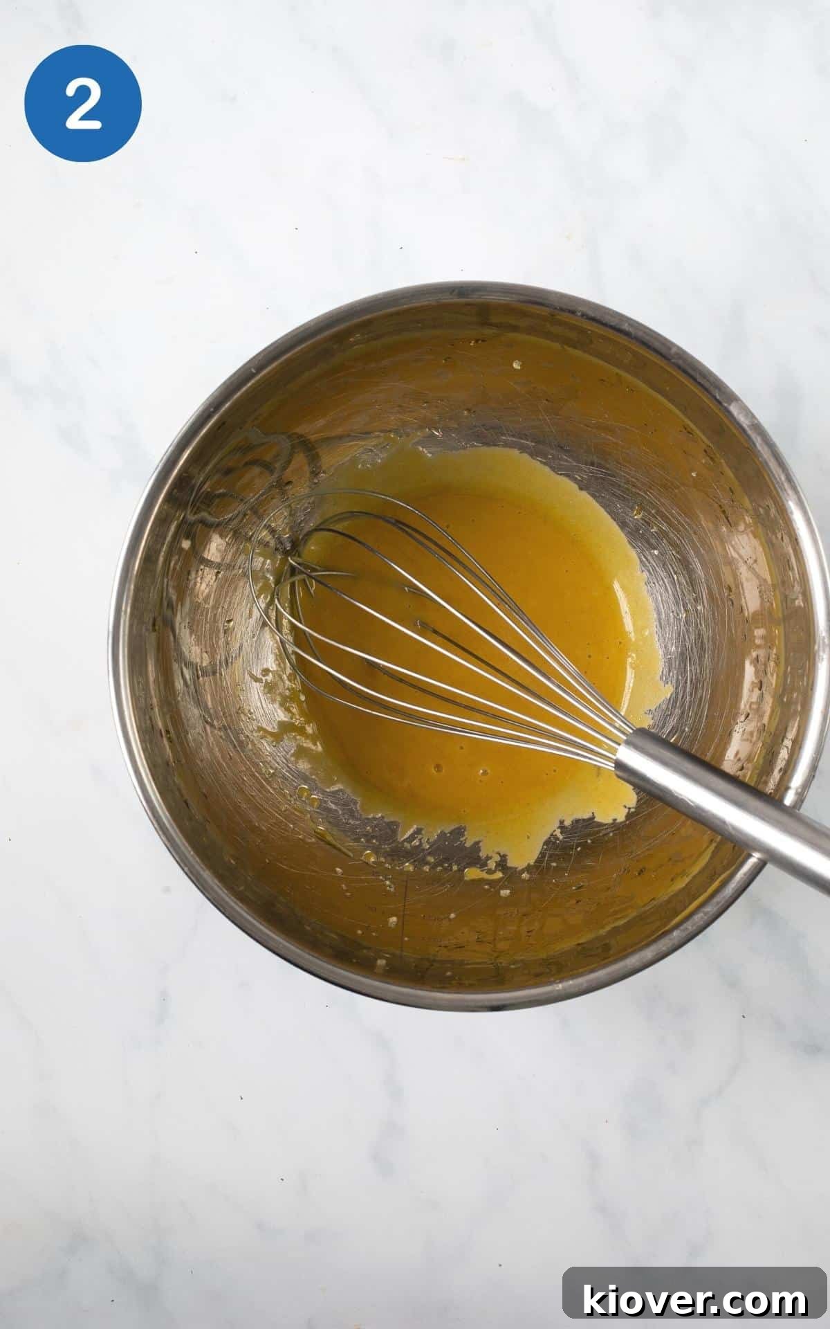 mustard, maple, olive oil, salt mixed in a silver mixing bowl with a whisk.