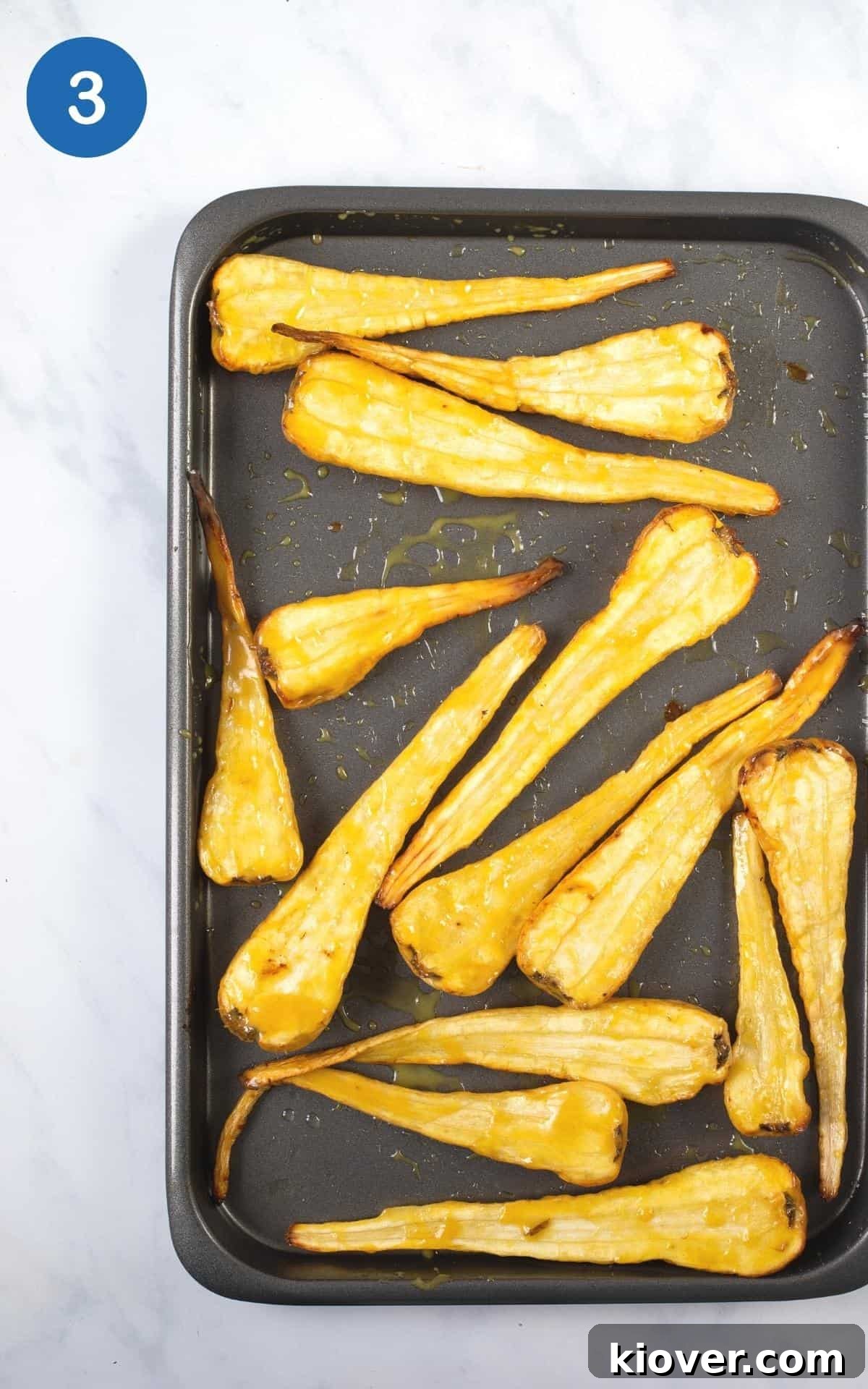 overhead view of these roasted parsnips on a grey baking tray ready to roast.