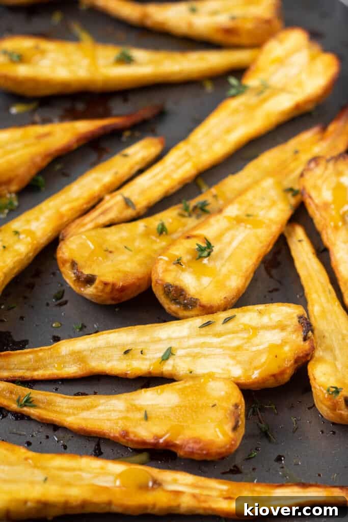 mustard and maple glazed parsnips close up front facing on baking tray with chopped thyme.