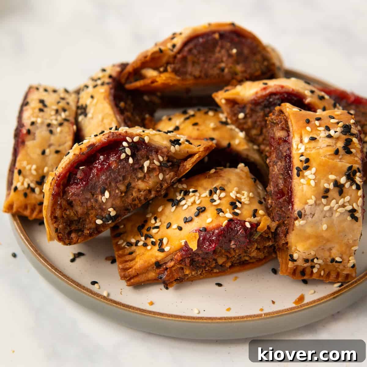 Crispy Vegan Sausage Rolls: Flaky Pastry with Savory Filling 2 homemade lentil and walnut sausage rolls on a stoneware plate garnished with sesame seeds.