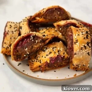Crispy Vegan Sausage Rolls: Flaky Pastry with Savory Filling 15 homemade lentil and walnut sausage rolls on a stoneware plate garnished with sesame seeds.