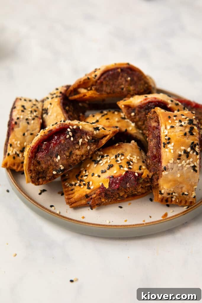 Crispy Vegan Sausage Rolls: Flaky Pastry with Savory Filling 10 homemade lentil and walnut sausage rolls on a stoneware plate garnished with sesame seeds.
