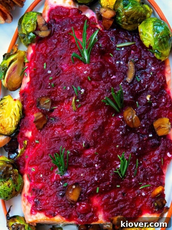 baked christmas salmon served with cranberry sauce and brussels sprouts on a white plate.