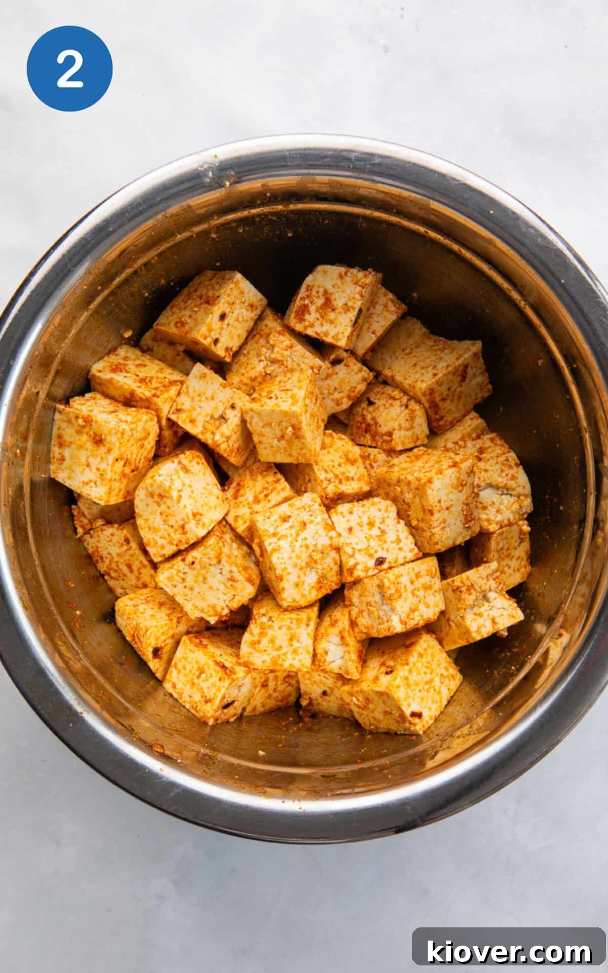 cubed tofu mixed with olive oil, paprika, onion powder, garlic powder, and red pepper flakes in a bowl.