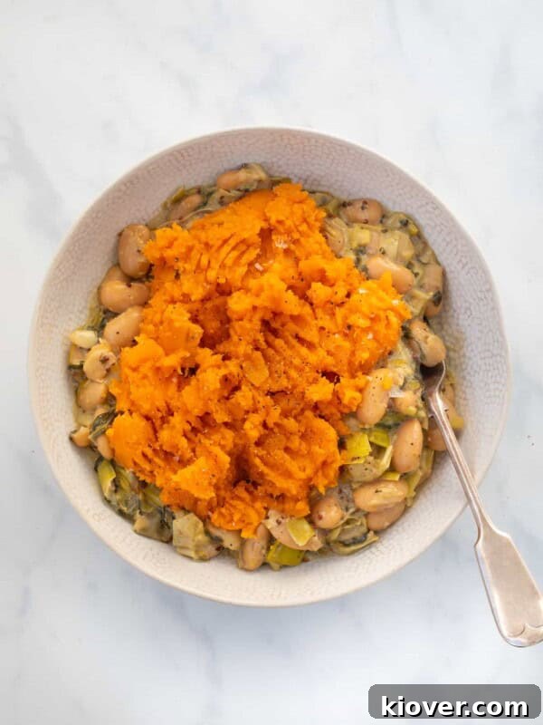 Savory Vegan Mushroom Pie Recipe with Flaky Crust 12 overhead view of this Gluten-Free and Vegan Butterbean and Leek Pie topped with sweet potato mash in a white bowl with a silver spoon on a marble countertop.
