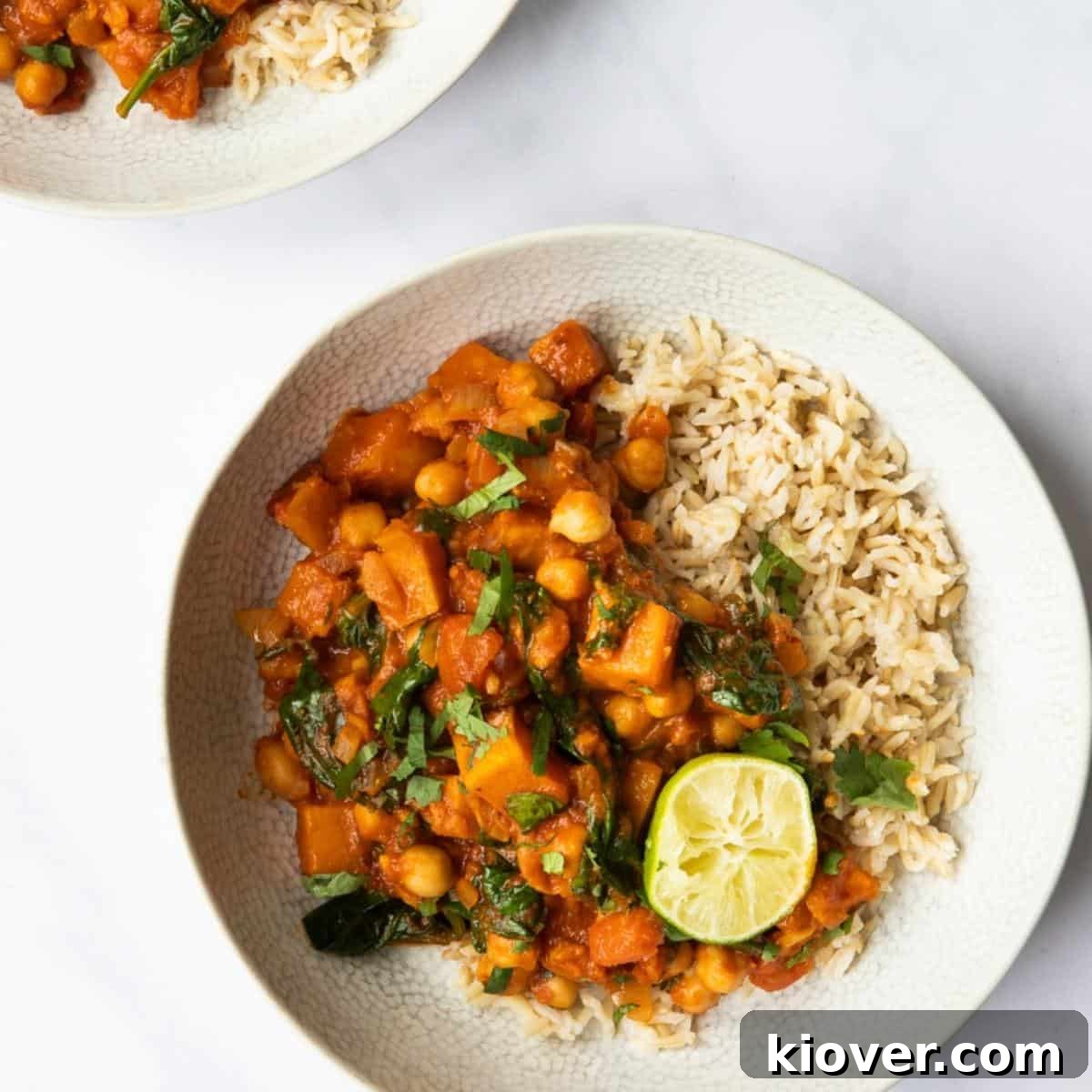 Butternut Squash and Chickpea curry served with rice in a bowl on a white marble background. 
