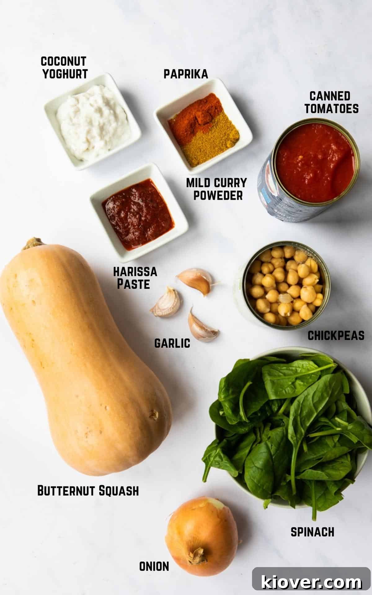 Ingredients to make a butternut squash and chickpea curry laid out on a white marble background. 