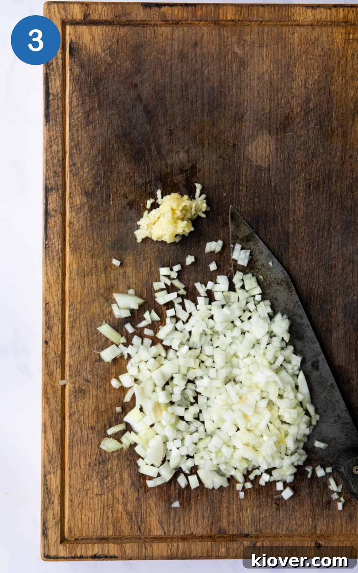 Finely diced garlic and onion on a wooden chopping board with knife.