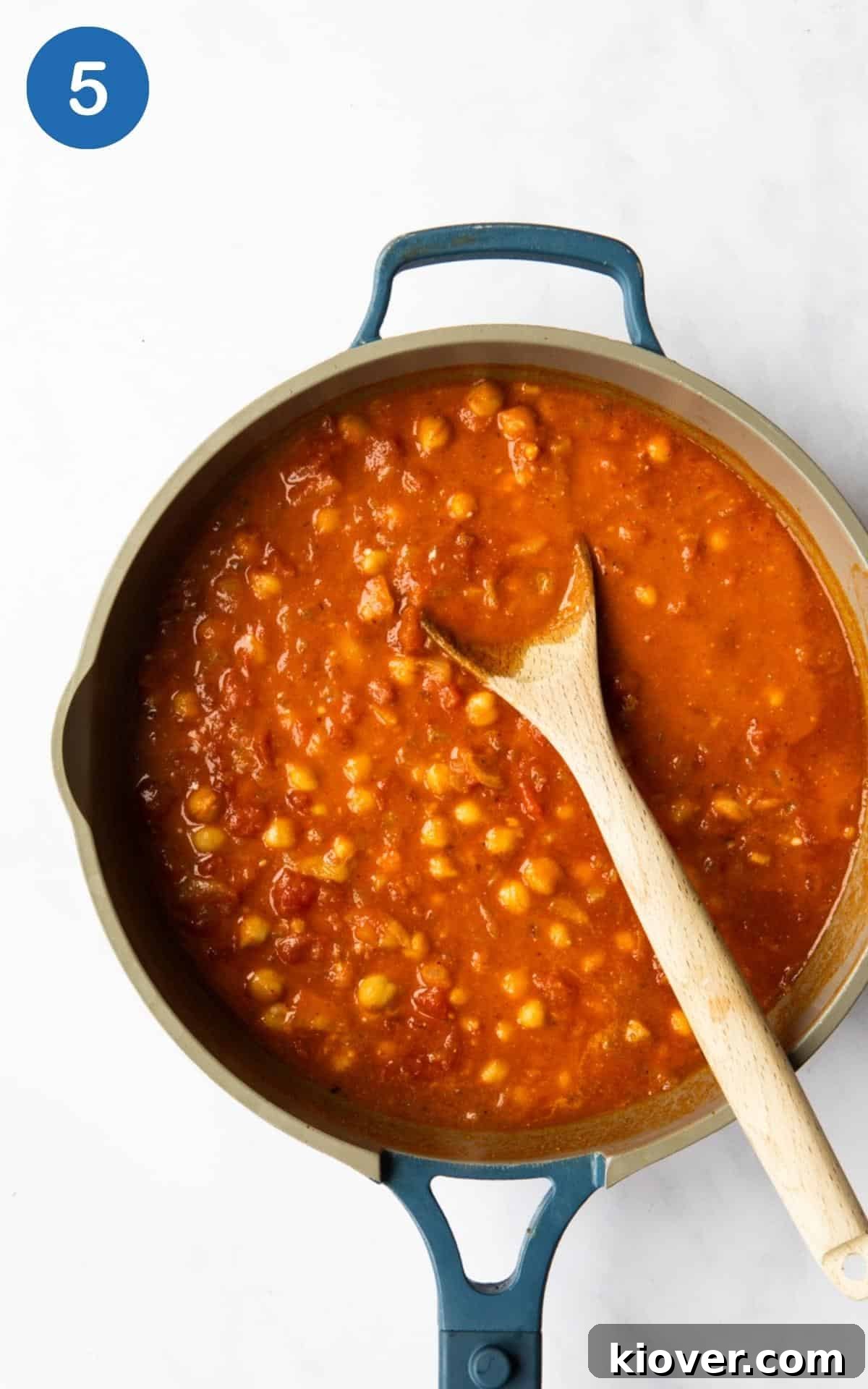 Butternut squash and chickpea curry being cooking in a frying pan with wooden spoon. 