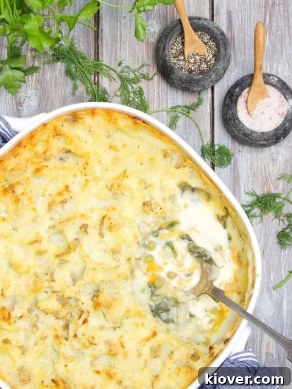 Fish pie being served with silver spoon on a wooden table. There is parsley to accessorise the table, along with small pots of of salt and pepper.