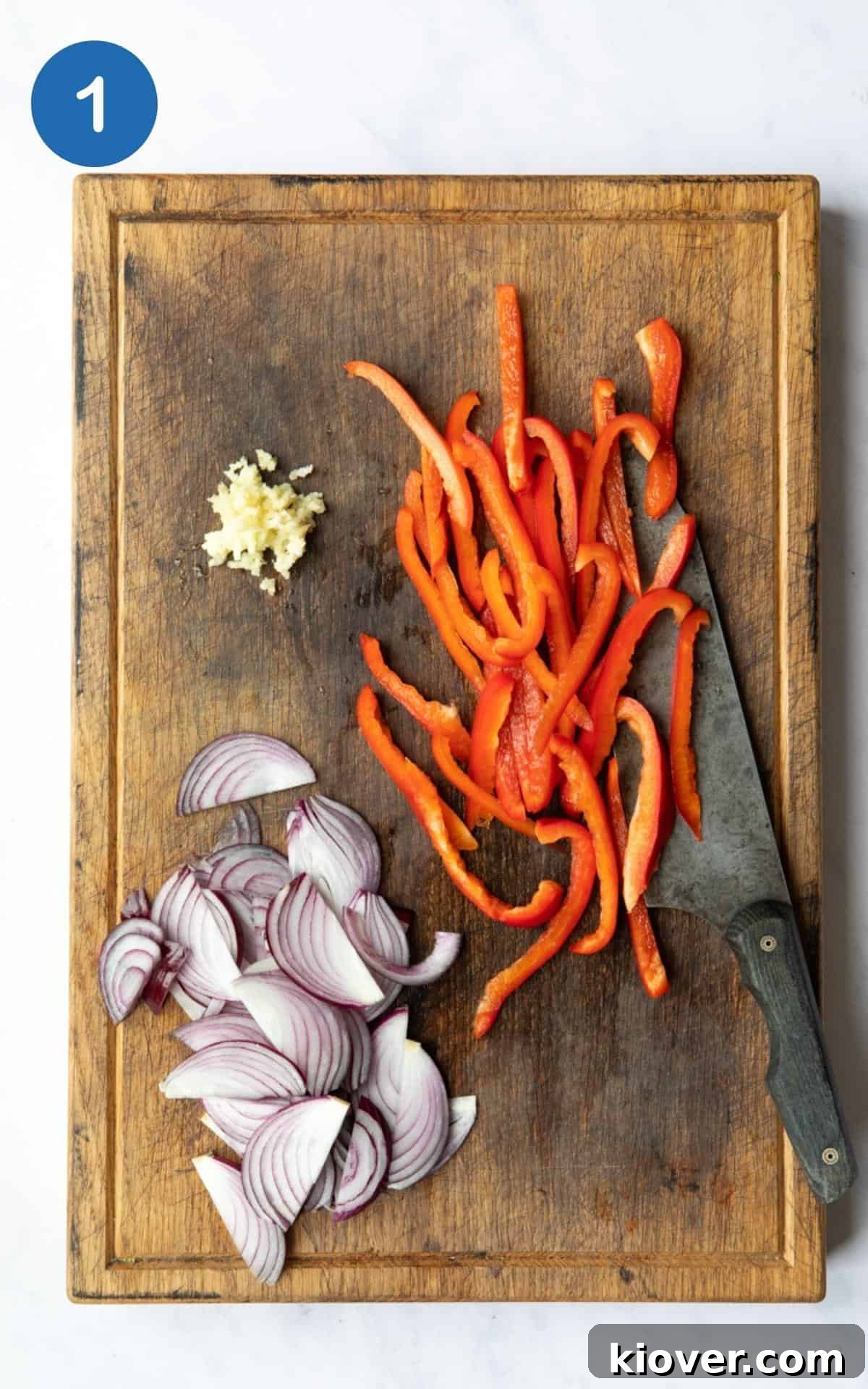 Thai Curry Noodle Soup Recipe — Creamy Thai Coconut Noodle Bowl 4 Sliced red pepper, onion and garlic laid out on a wooden chopping board with a knife.