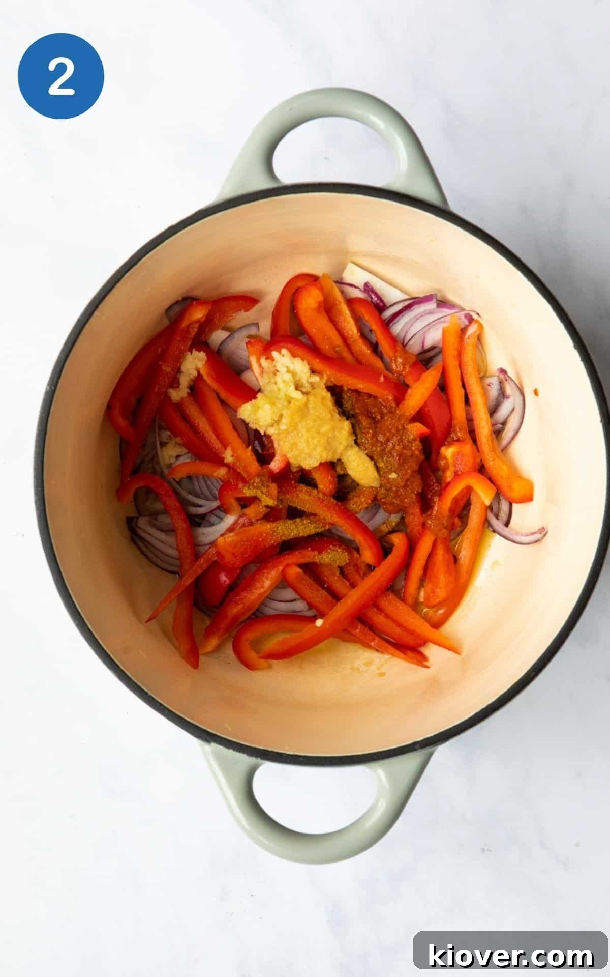 Thai Curry Noodle Soup Recipe — Creamy Thai Coconut Noodle Bowl 5 Onion, red pepper, garlic, red thai curry paste, curry powder, ginger paste in a large pot before cooking, displayed on a white marble background.