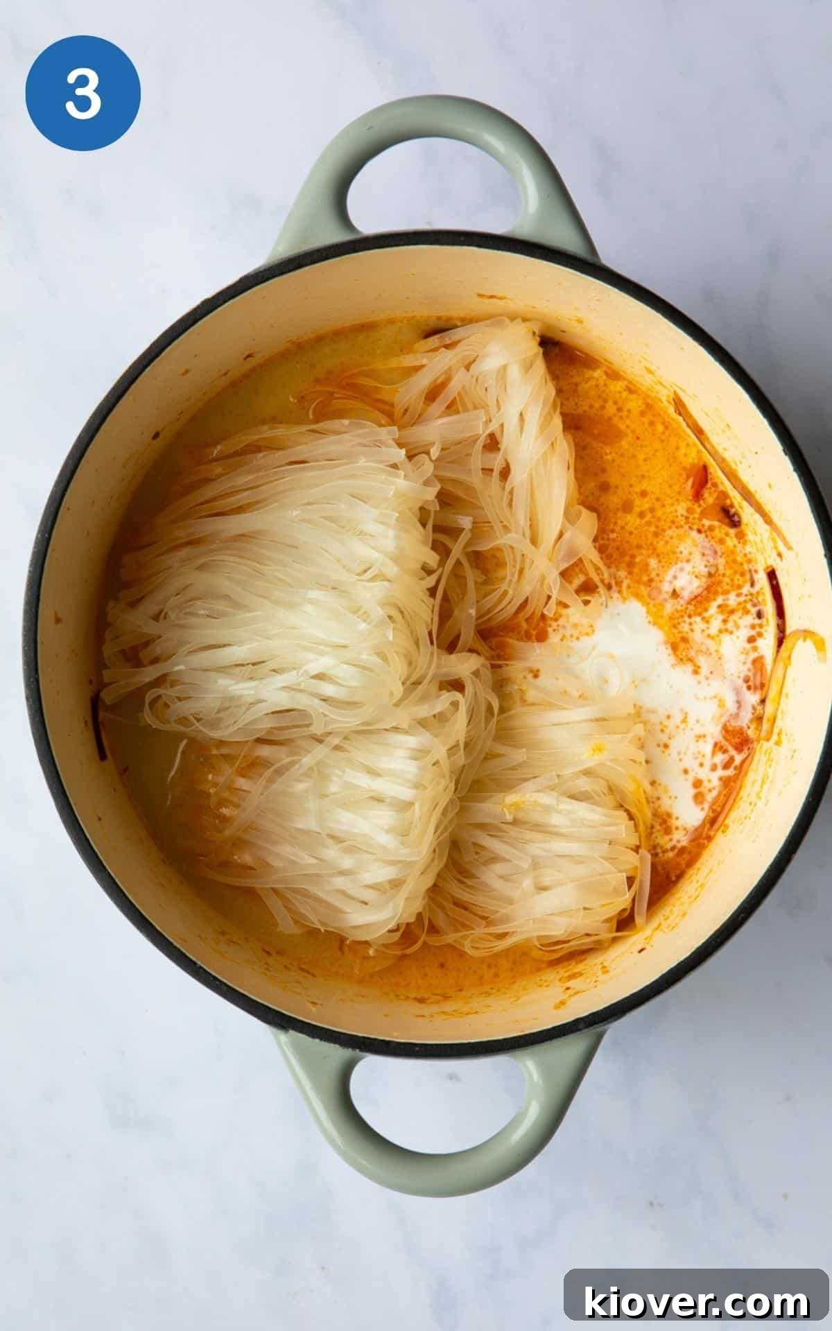 Thai Curry Noodle Soup Recipe — Creamy Thai Coconut Noodle Bowl 6 Thai Curry Noodle Soup being cooked in a large pot, coconut milk, water, stock, and noodle have just been added. Pot is displayed on a white marble background.