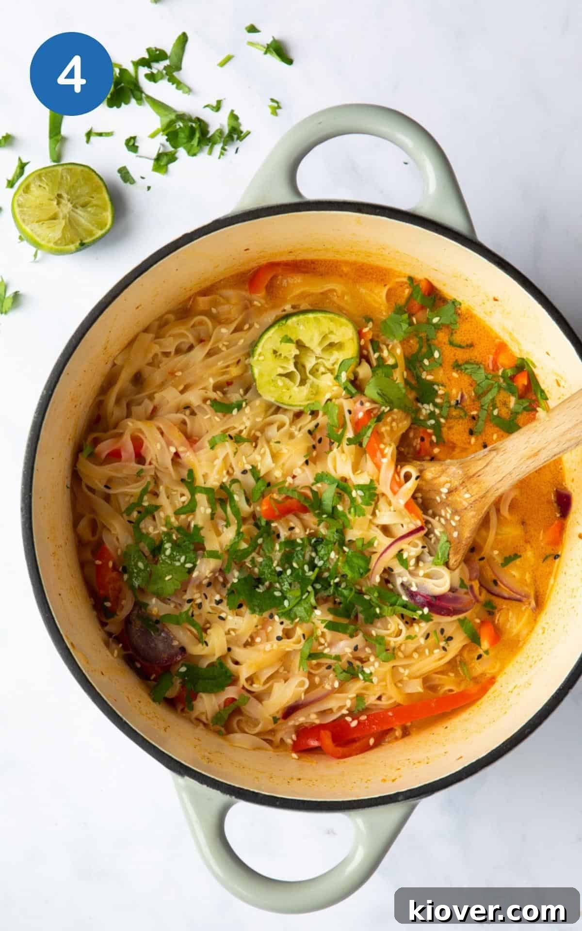 Thai Curry Noodle Soup Recipe — Creamy Thai Coconut Noodle Bowl 7 Thai Curry Noodle Soup served in a large cast iron pot served with lime and fresh coriander on white marble.